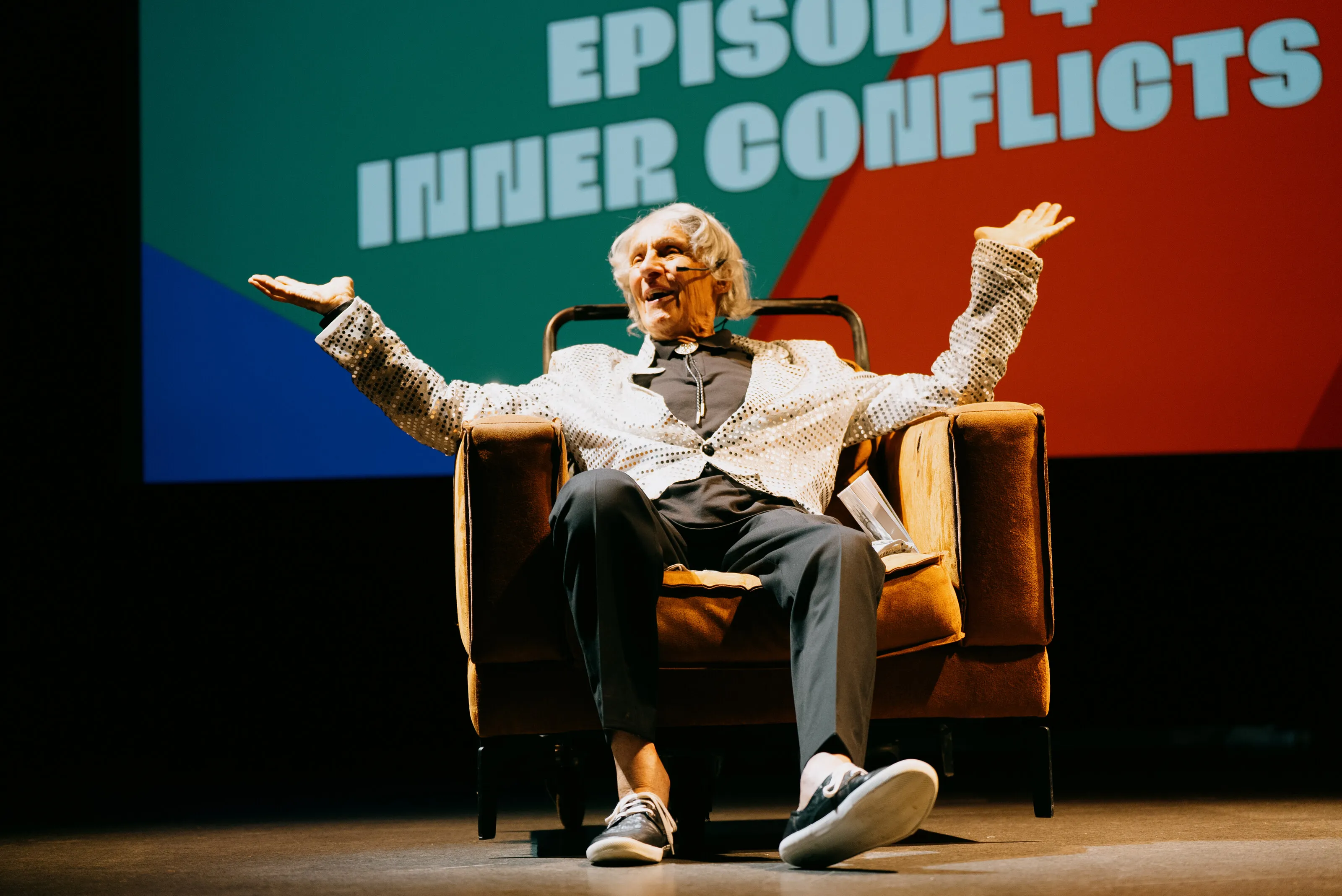 Ein älterer Darsteller sitzt mit ausgebreiteten Armen vor der Projektion «Inner Conflicts».