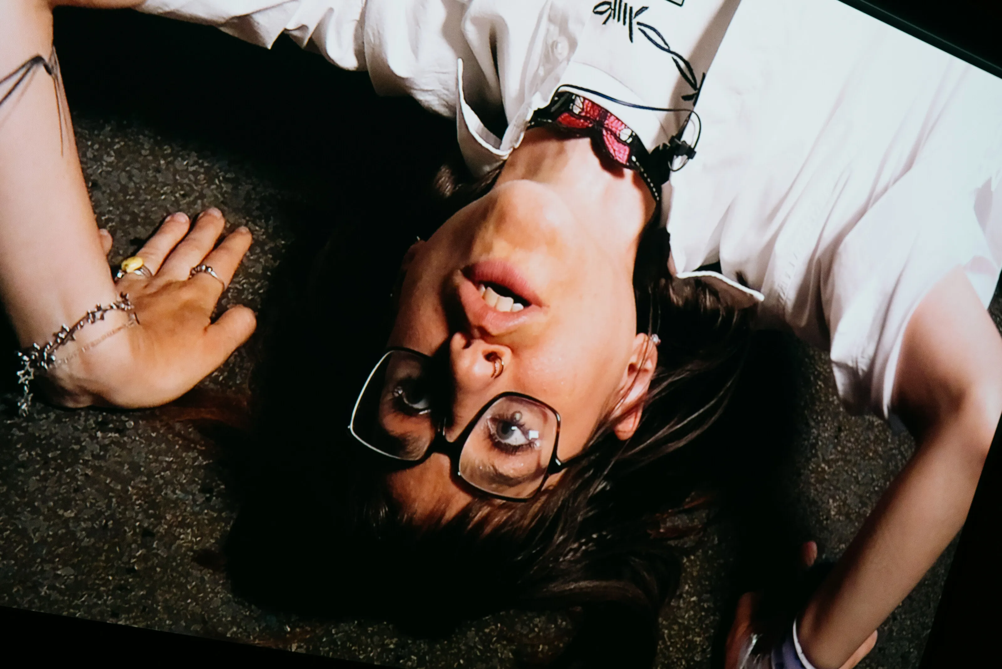 Eine Darstellerin mit Brille liegt kopfüber im Licht vor einer Videoprojektion.